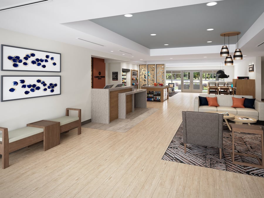 A modern hotel lobby with a reception desk, seating area, and a view of the outdoors.