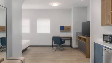 Habitación de hotel pequeña con cama, escritorio, silla, televisor, microondas y un mueble bajo.