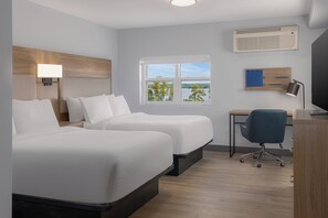 A hotel room with two beds, a desk, a chair, a TV, and a window with a view of trees and water.