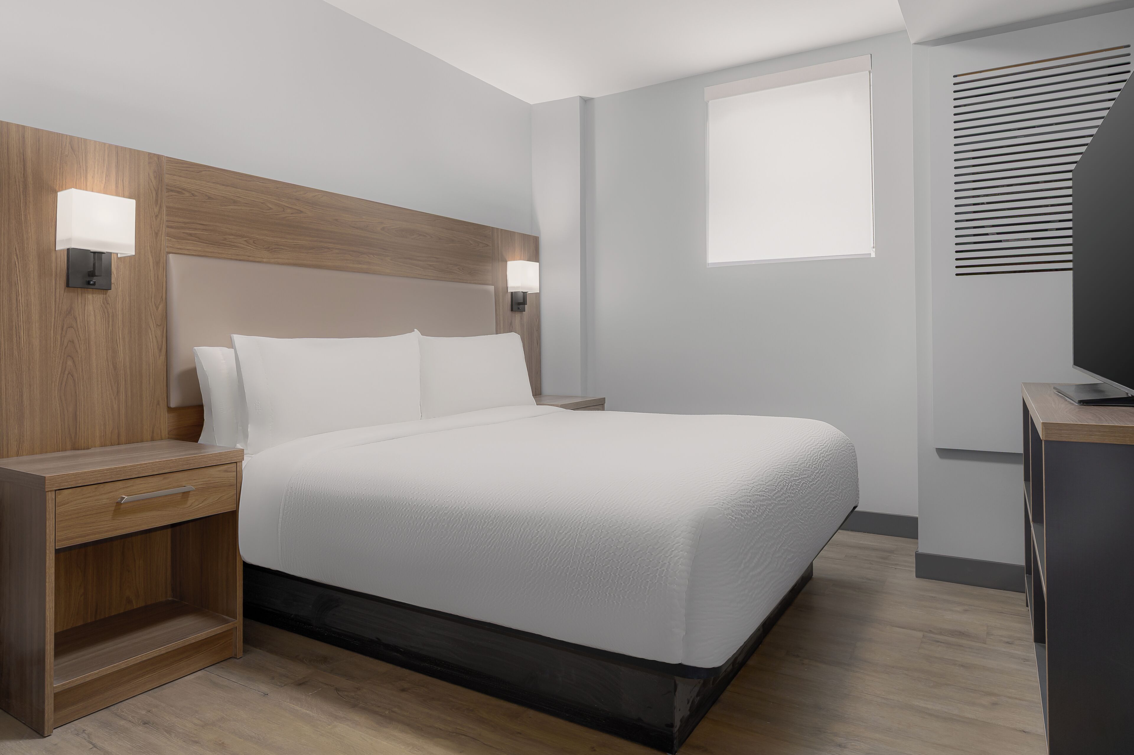 Et moderne hotelværelse med en stor seng, sengeborde, et skrivebord og et fjernsyn.