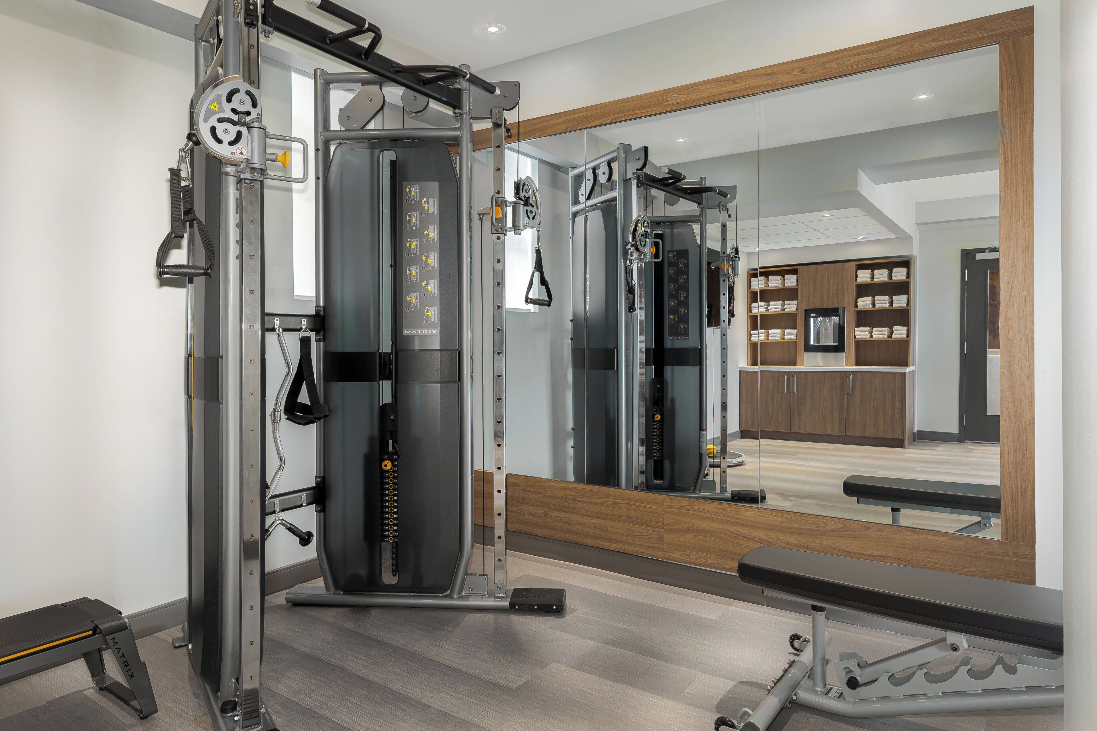 A gym with a mirrored wall, weightlifting equipment, and a bench.
