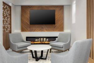 Una sala de estar moderna con un televisor de pantalla plana montado en una pared de madera, una chimenea y sillones grises alrededor de una mesa de centro redonda.