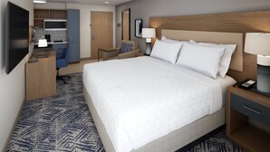 Quarto de hotel com uma cama grande, uma escrivaninha, uma cozinha compacta e uma televisão.