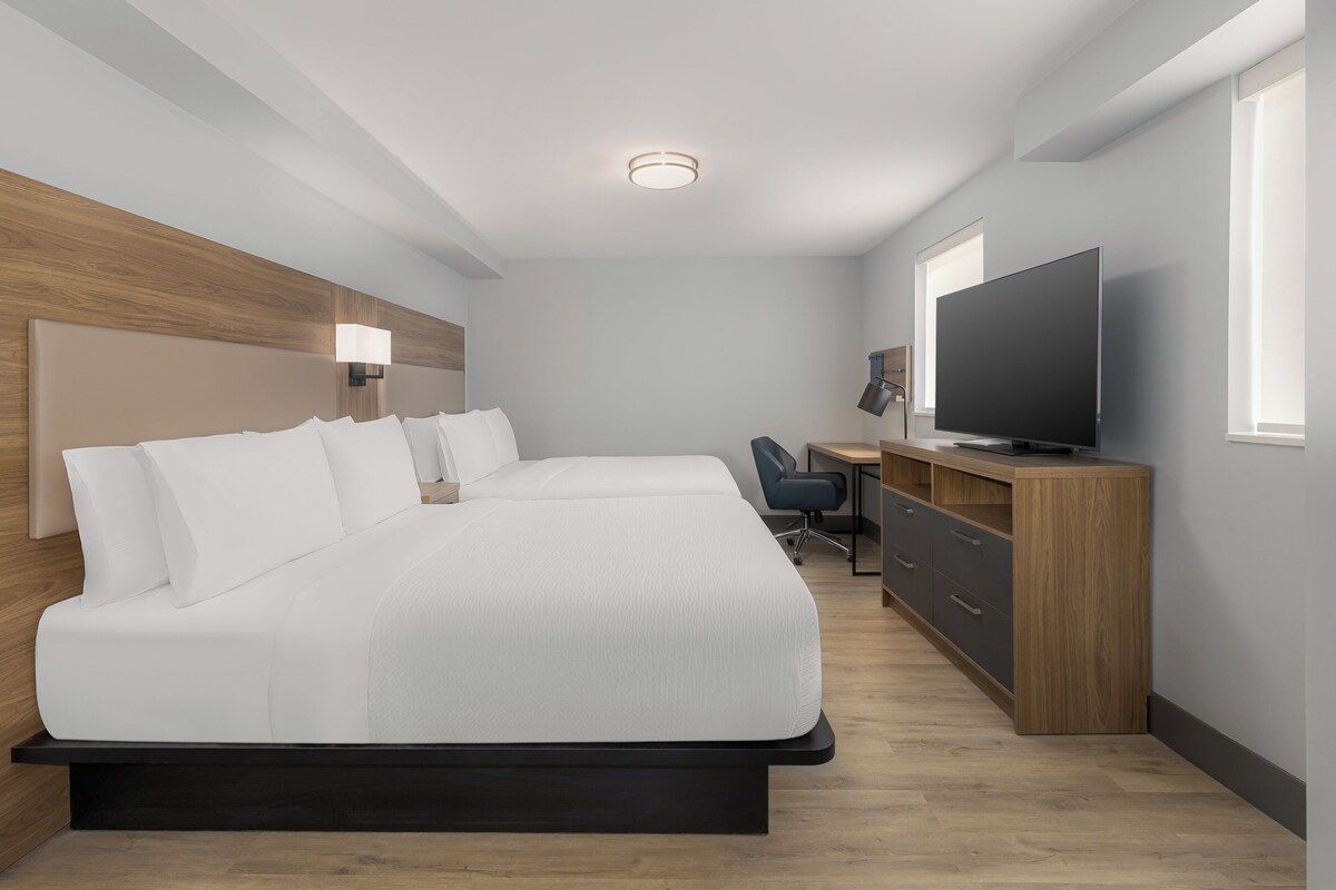Quarto de hotel moderno com uma cama grande, uma escrivaninha, uma cadeira, uma televisão e uma janela.