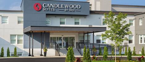 A hotel entrance with a modern design, featuring a prominent logo and the name 'CANDLEWOOD SUITES BY IHG' above the entrance.