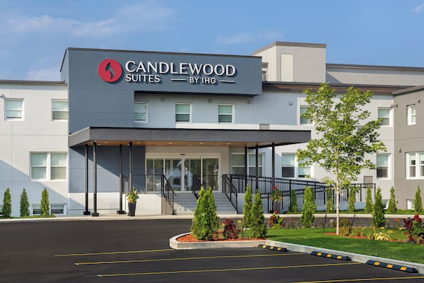 Entrada de un hotel con diseño moderno, que presenta un logotipo destacado y el nombre 'CANDLEWOOD SUITES BY IHG' sobre la entrada.