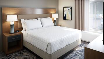 Une chambre d’hôtel avec un grand lit, deux tables de chevet avec des lampes, une tête de lit, une fenêtre avec des rideaux et une œuvre d’art abstraite accrochée au mur.