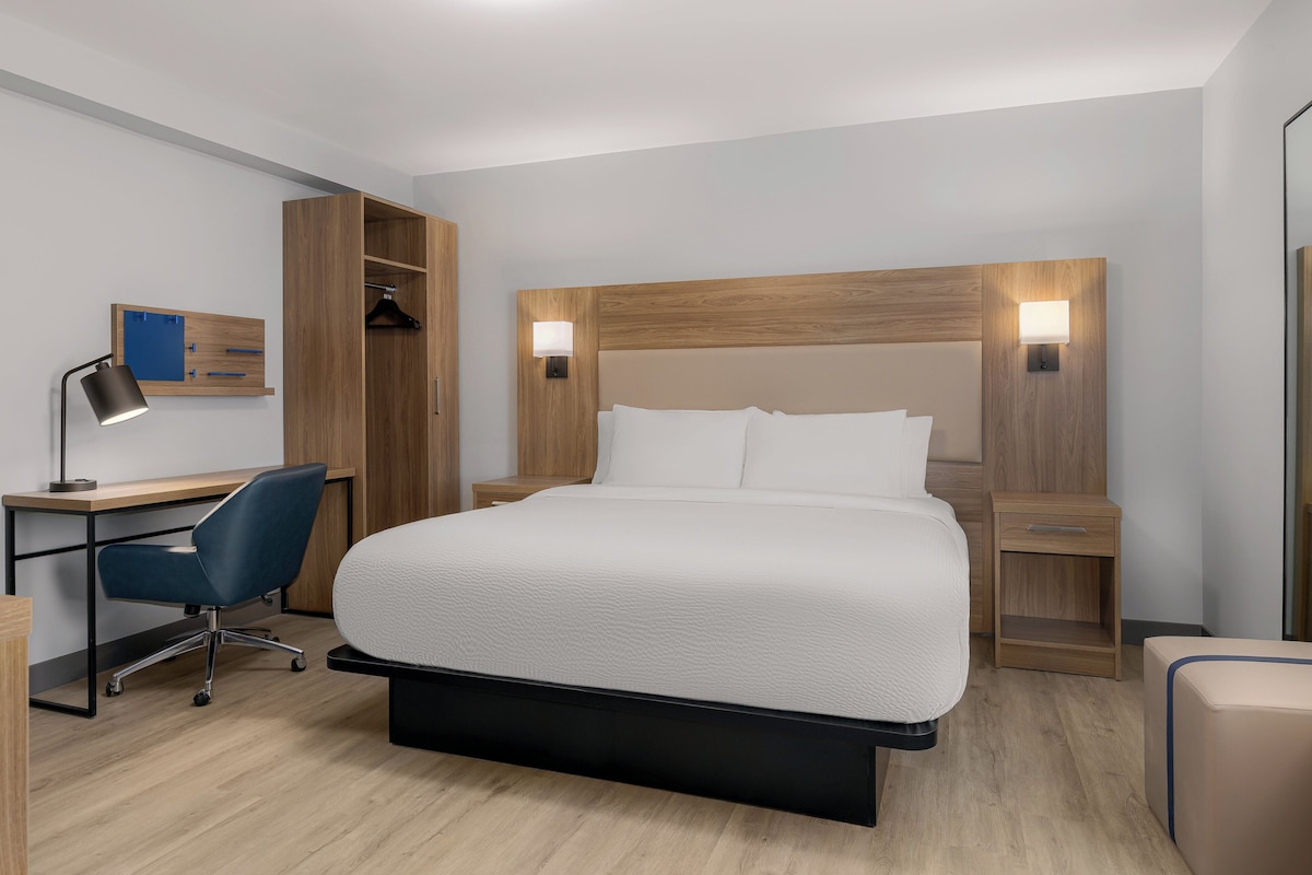 Quarto de hotel com cama, escrivaninha, cadeira, guarda-roupa e mesas de cabeceira.