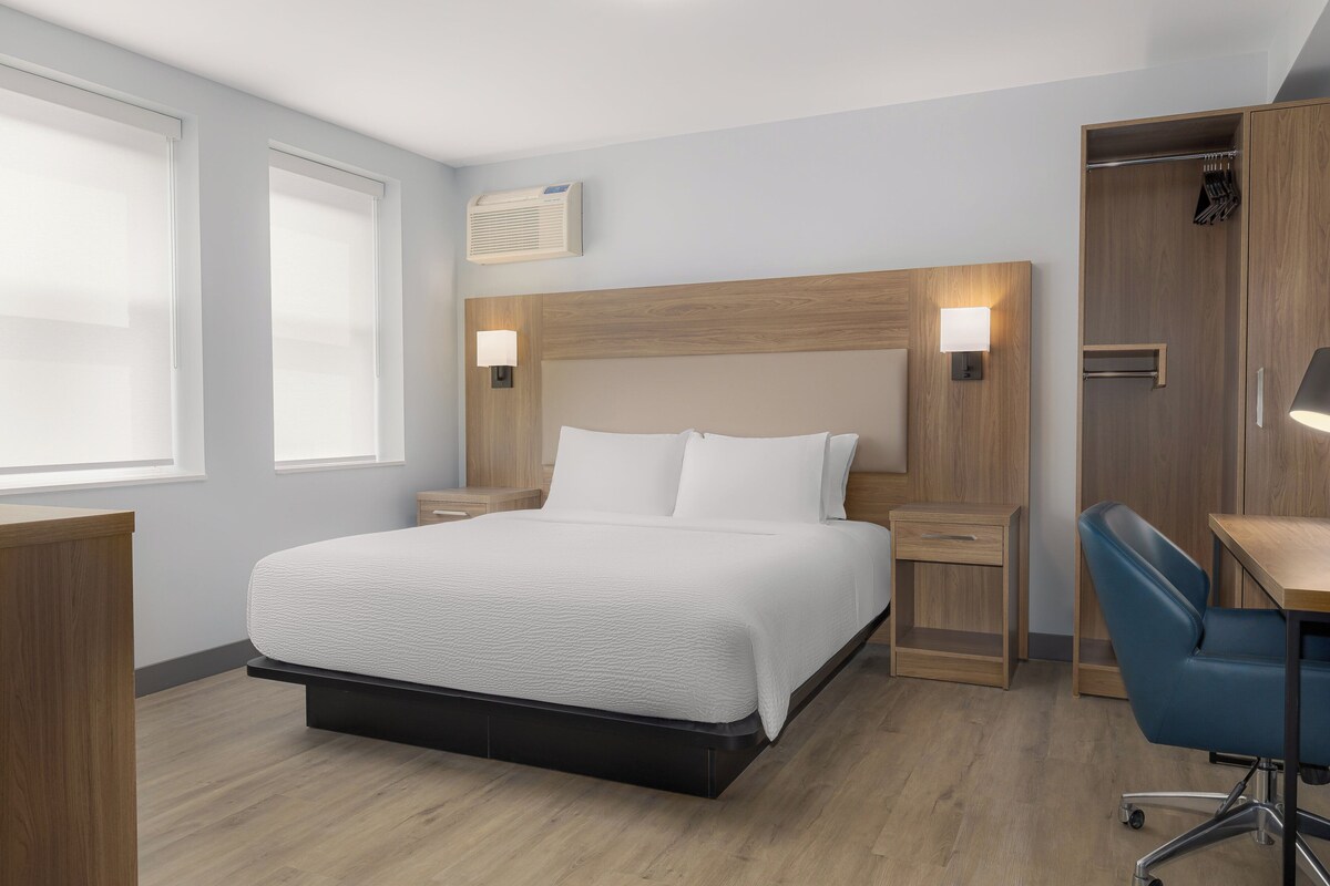 Quarto de hotel com cama, mesas de cabeceira, escrivaninha com cadeira e guarda-roupa.