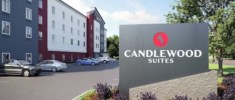Een hotelschiltje met 'CANDLEWOOD SUITES' en een modern gebouw op de achtergrond.