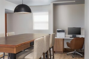A modern office space with a wooden conference table, leather chairs, a desk with a computer and printer, and a large window providing natural light.