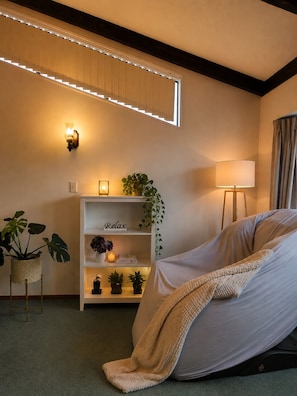 Une pièce comprenant un lit, une étagère avec des plantes, un luminaire fixé au mur et un lampadaire.