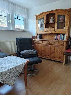Ein Wohnzimmer mit einem Holzschrank, einem schwarzen Ledersessel, einem Tisch mit Blumenmuster und einer Heizung.