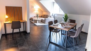 A modern dining area with a table set for two, a sofa in the background, and a lamp on a side table. - Premium City Apartment (Braunschweig)