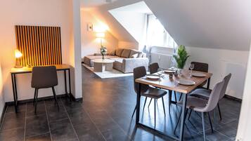 A modern dining area with a table set for two, a sofa in the background, and a lamp on a side table.