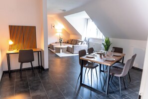 A modern dining area with a table set for two, a sofa in the background, and a lamp on a side table. - Premium City Apartment (Braunschweig)