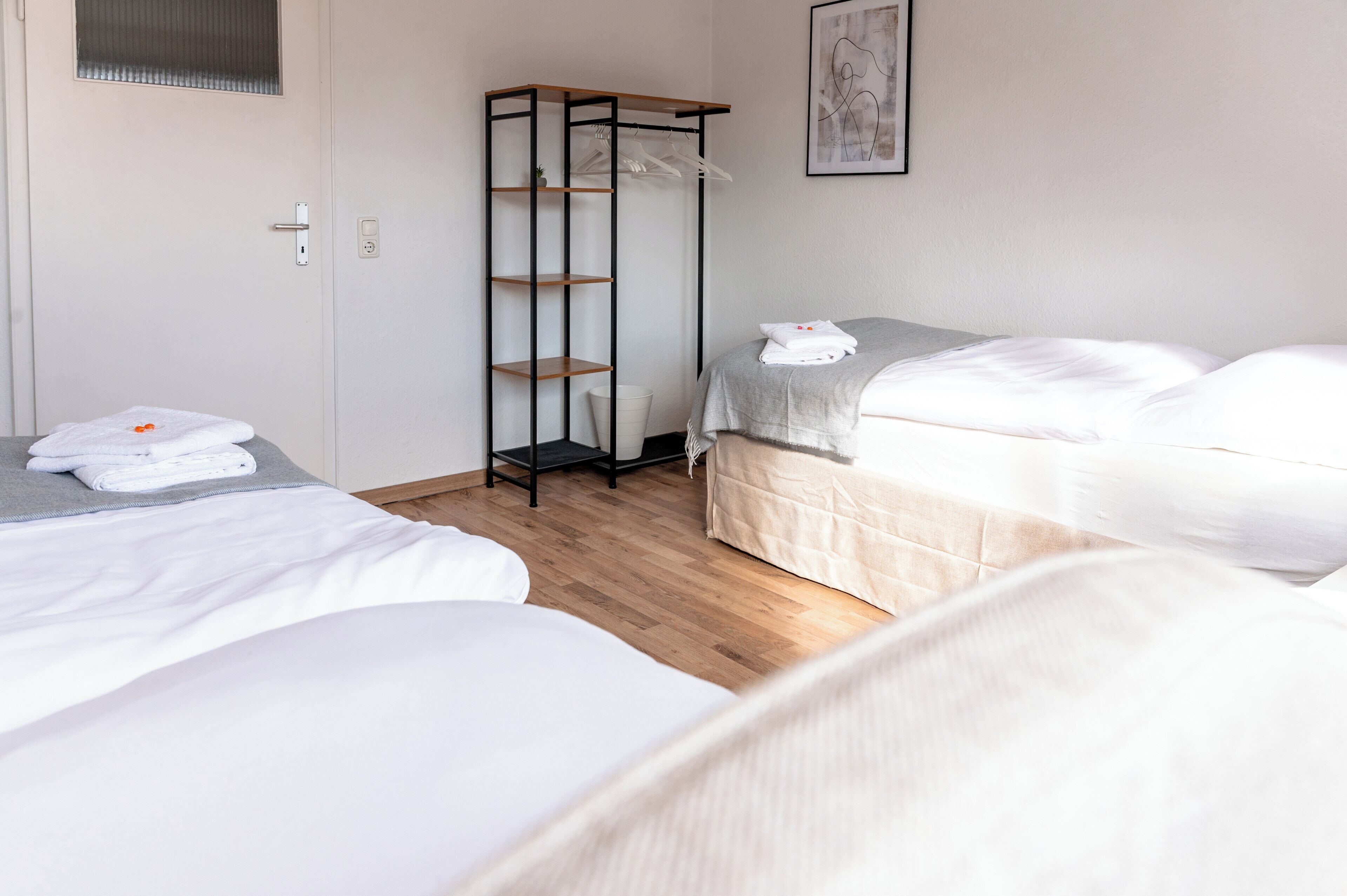 A hotel room with two beds, a wardrobe, a small table, and a painting on the wall.