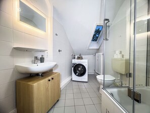 Ein modernes Badezimmer mit Waschbecken, Toilette, Waschmaschine und einer Duschkabine aus Glas.