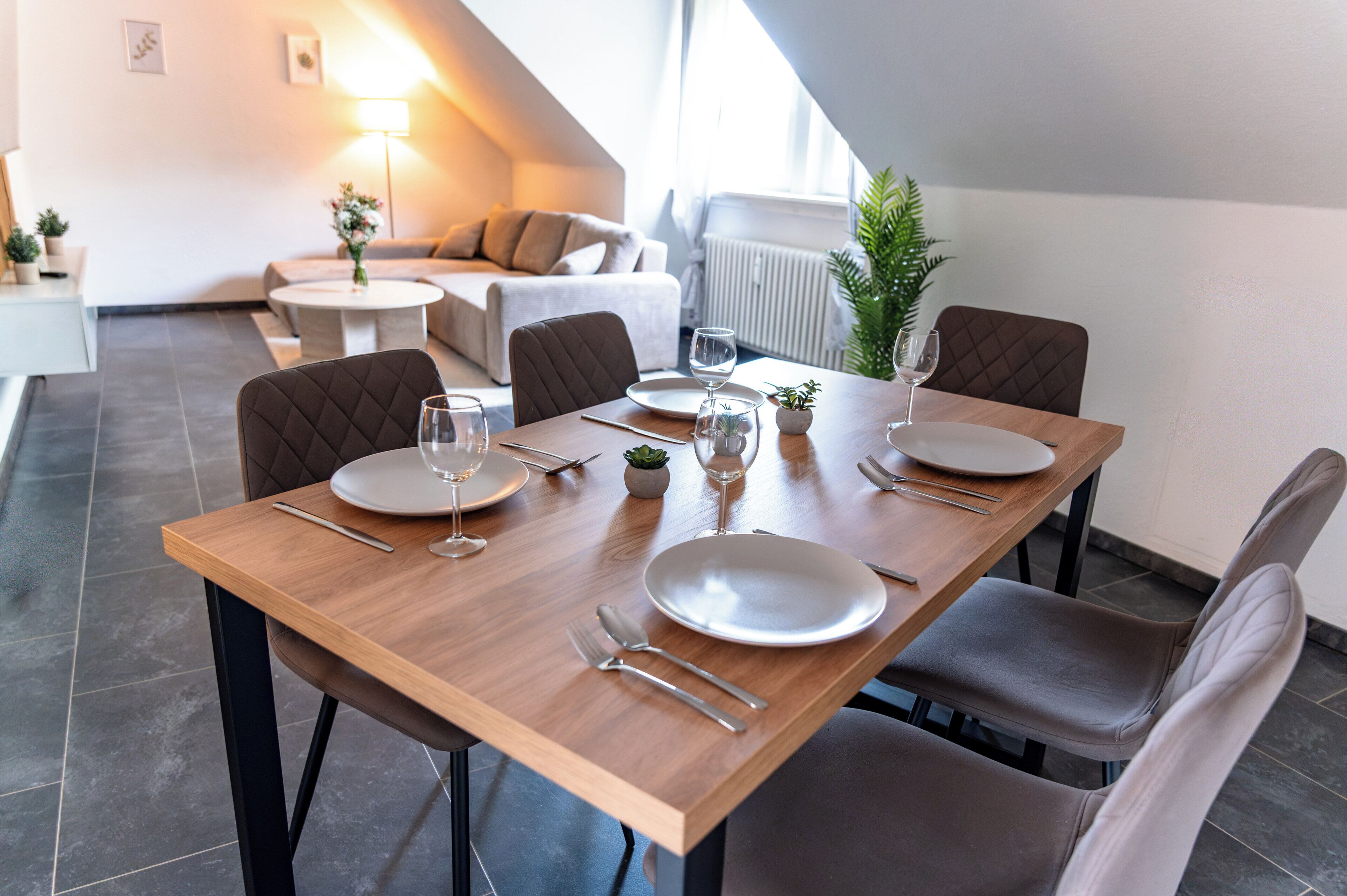 Een eetgedeelte met een houten tafel gedekt voor vier personen, inclusief borden, bestek en glazen.