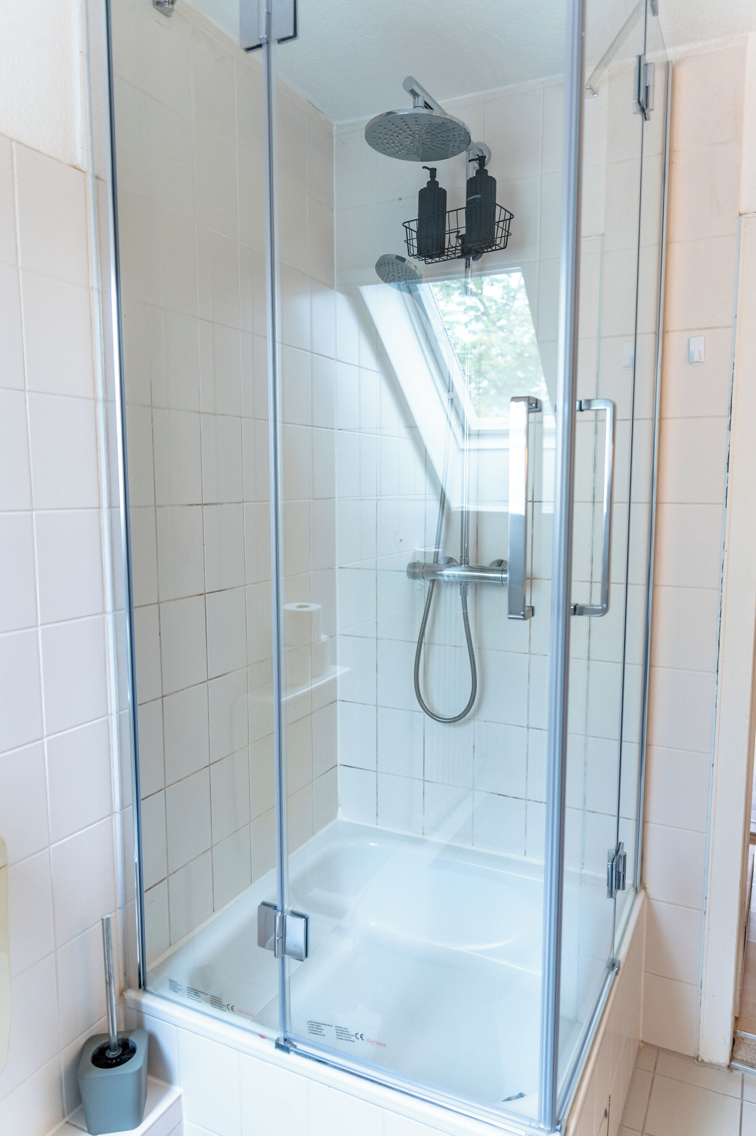 A glass-enclosed shower with a handheld showerhead and a wall-mounted faucet.