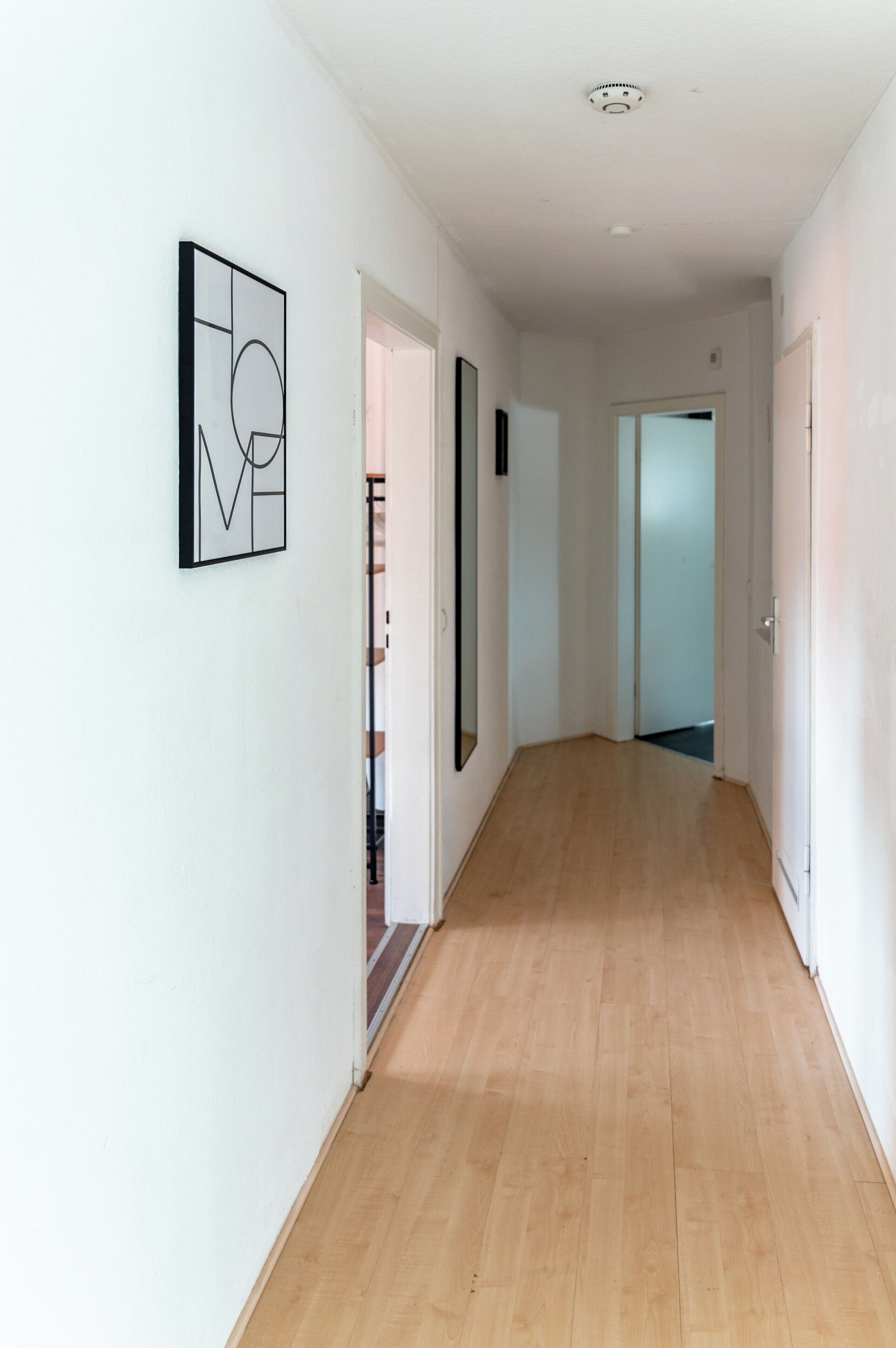 Een gang met een houten vloer, witte muren en een deur naar een andere kamer.
