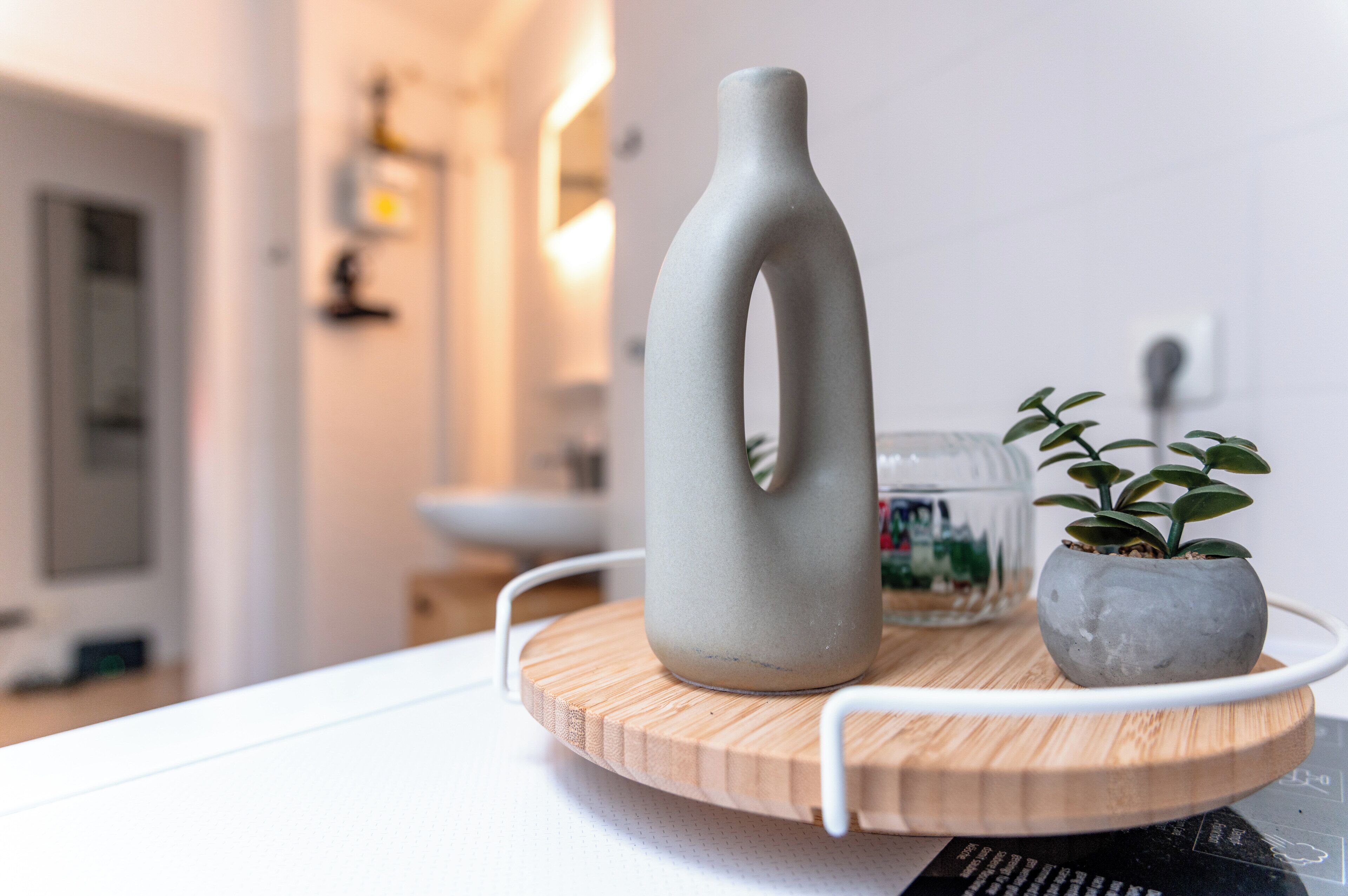 Een moderne keuken met een houten snijplank, een keramieken vaas en een potplant op een wit aanrecht.
