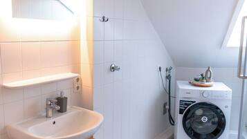 A modern bathroom with a white sink, wooden cabinet, and a washing machine.