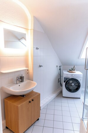 A modern bathroom with a white sink, wooden cabinet, and a washing machine. - Premium City Apartment (Braunschweig)