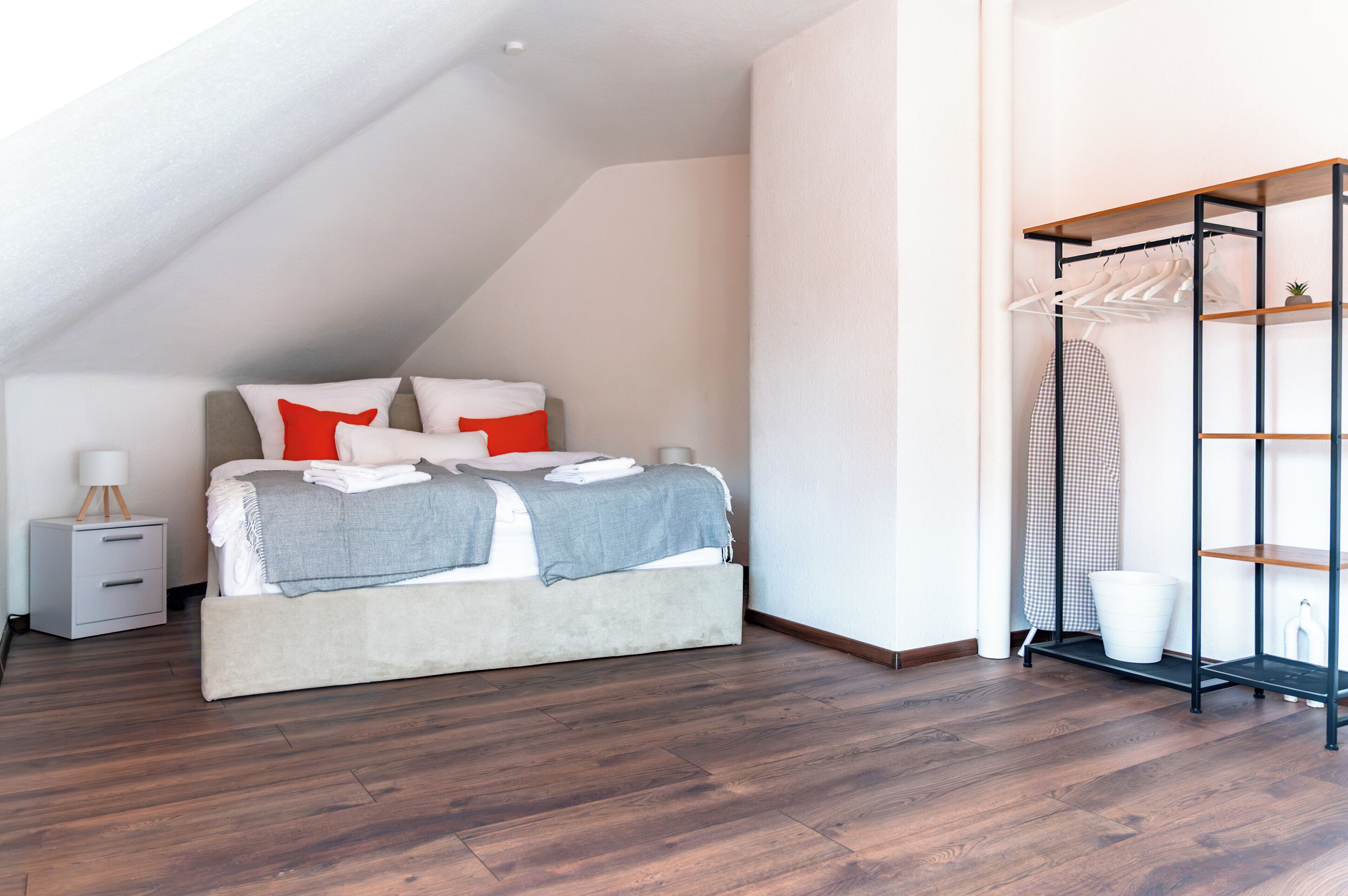 A bedroom with a bed, a nightstand, a hanging clothes rack, and a white wall.
