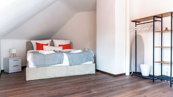 A bedroom with a bed, a nightstand, a hanging clothes rack, and a white wall.