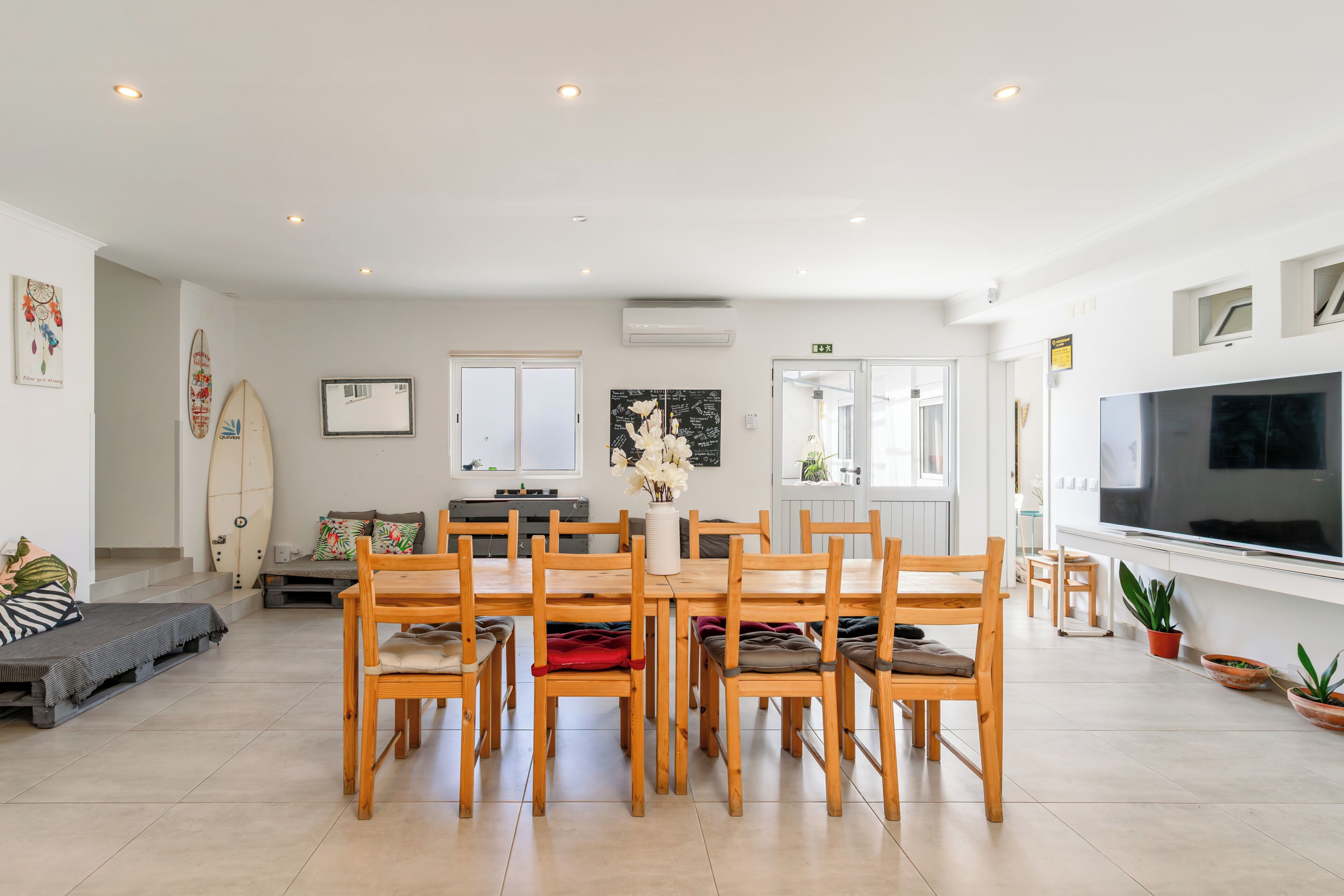 Un comedor con mesa y sillas de madera, un televisor y una tabla de surf en la pared.