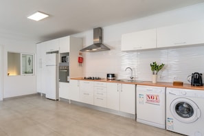 A modern kitchen with white cabinets, a stainless steel range hood, a washing machine, and a sink. - Beautiful 6 bedroom villa just 200 meters from costa caparica beach. (Costa de Caparica)