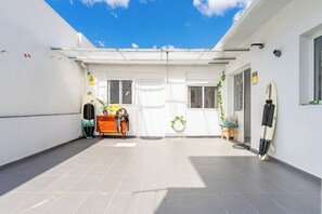 A covered outdoor area with a tiled floor, a surfboard leaning against the wall, and a potted plant near the entrance. - Beautiful 6 bedroom villa just 200 meters from costa caparica beach. (Costa de Caparica)