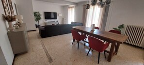 Ein Wohnzimmer mit einer Couch, einem Fernseher, einem Esstisch mit Stühlen und einer Heizung.