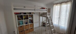 Ein Zimmer mit Etagenbett, einer Leiter, einem Bücherregal und einem Fenster mit Vorhängen.