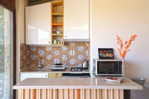 Una cocina con microondas, cafetera y un jarrón decorativo con flores naranjas.