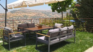 Un área de estar al aire libre con mesa y sillas, un toldo y vistas a un paisaje montañoso.