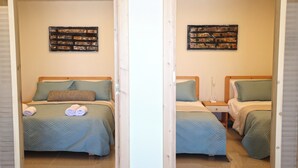 Una habitación con dos camas, cada una con cubrecama acolchado y almohadas, un cabecero de madera, una mesita de noche con lámpara y una obra de arte colgada en la pared.