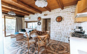 Un interior rústico con pared de piedra, vigas de madera en el techo, una zona de comedor con suelo de mosaico y una cocina con estufa a gas.