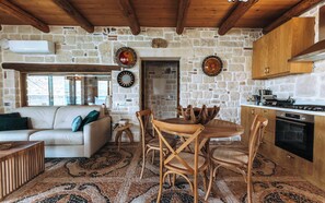 A cozy interior with a stone wall, wooden furniture, a dining table, and a kitchen area. - Apartment Minoa – Seafront Apartment next to Villa Minoa (Marathi)