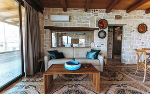 Una sala de estar acogedora con una pared de piedra, un sofá con cojines, una mesa de centro de madera con un cuenco y una alfombra estampada.
