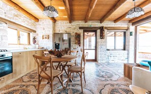 A rustic kitchen with stone walls, wooden beams, a tiled floor, and a dining area with wooden chairs and a table. - Apartment Minoa – Seafront Apartment next to Villa Minoa (Marathi)