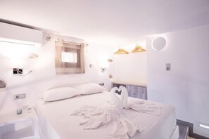 A modern hotel room with a neatly made bed, a bedside table, a wall-mounted light, and a circular light fixture. - Primrose Apartments  (Astypalaia)
