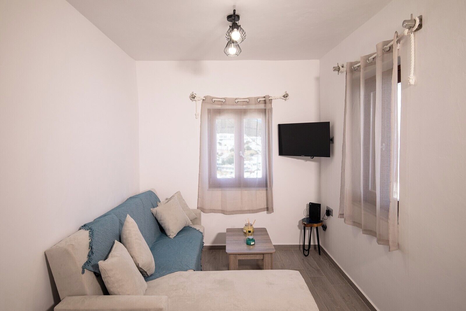 A bedroom with a bed, a TV, a window with curtains, and a small table with a lamp.