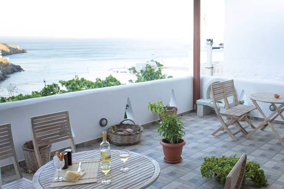 A terrace with a round table, chairs, a potted plant, and a view of the sea.
