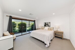 Un dormitorio con una cama grande, una mesita de noche, una silla y una ventana con cortinas.