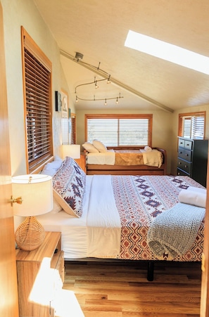 Un dormitorio acogedor con techo inclinado, una cama con ropa de cama estampada, una lámpara de noche y un aparador.