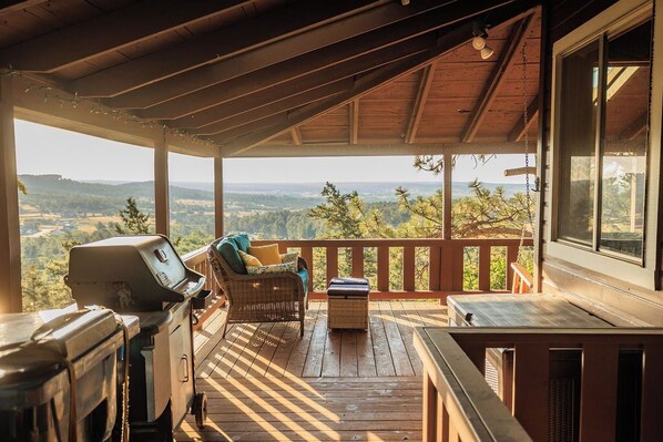 Un espace extérieur abrité, équipé d’un barbecue, de meubles en osier et offrant une vue sur le paysage.