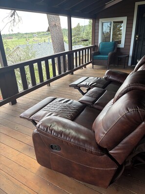 A brown leather sofa with a built-in massage function, a wicker chair, and a view of a green landscape.