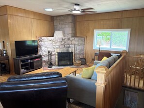 A living room with a stone fireplace, a television, a sofa, and a wooden ceiling fan.